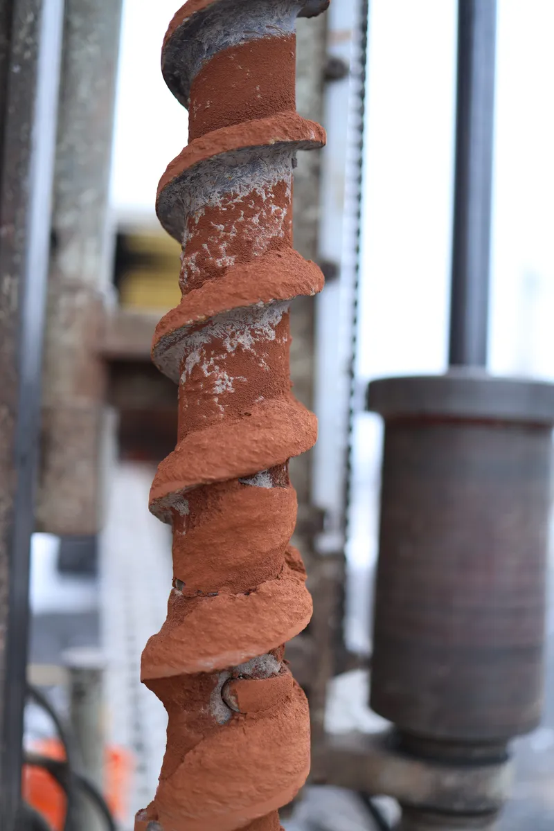 Auger flight lifted from the hole, caked with clay