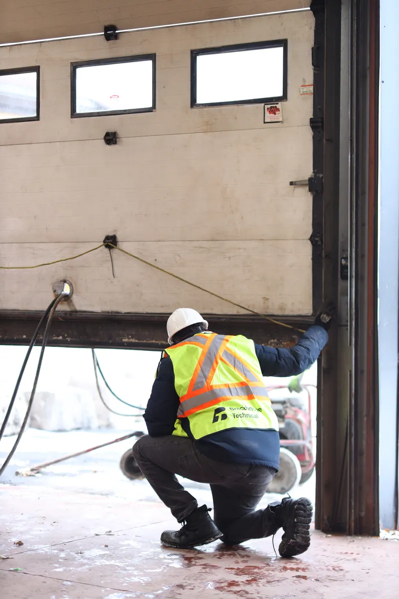 Crouched in an open bay door, marked hi-vis, daylight beyond