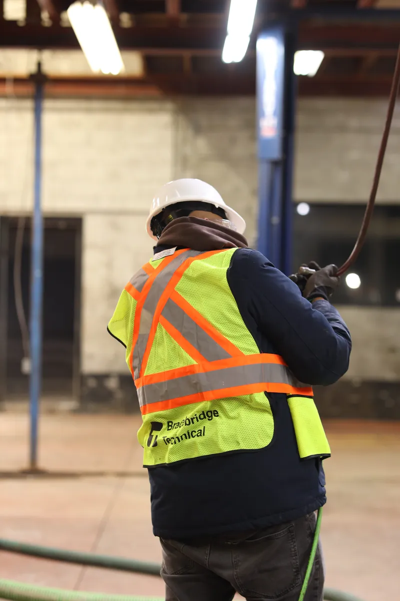 A marked hi-vis back, suction hose held overhead in a service bay