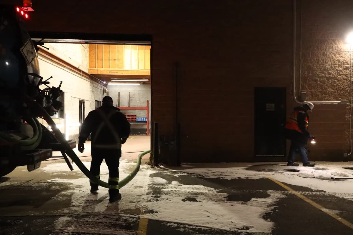 A vacuum truck at an open bay door before dawn, hose run inside